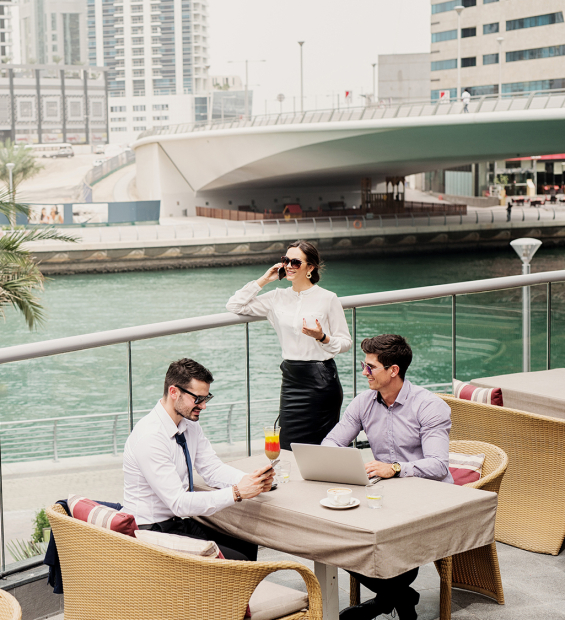 Three young business colleges taking a break in a Dubai Marine .Sitting on a balcony and talking.