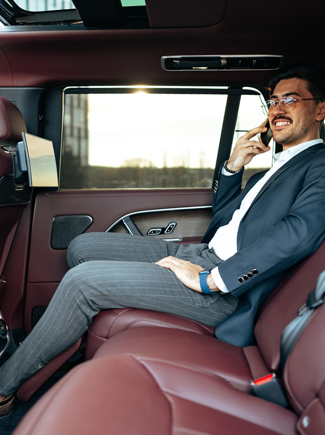 Young businessman in suit and glasses sitting on passenger seat in a luxury car close up